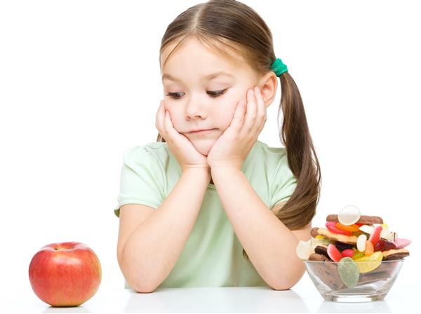 دختر کوچک ناز که از سیب و شیرینی انتخاب می کند بیش از سفید جدا شده است