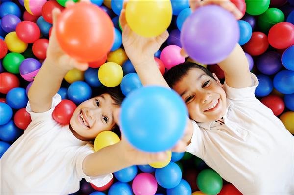 کودکان خوشبختی که با هم و با توپ های رنگارنگ در کودکستان بازی می کنند و از آن لذت می برند