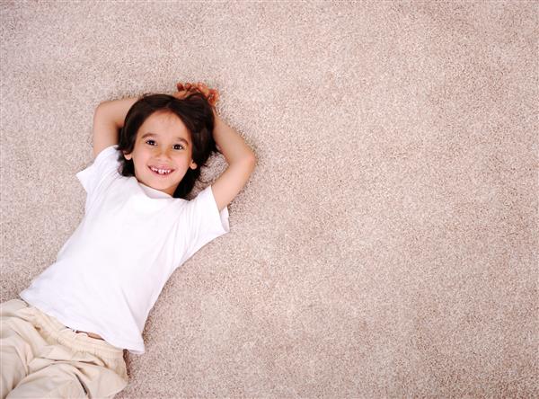 پسر کوچک در خانه روی کف فرش خوابیده و لبخند می زند