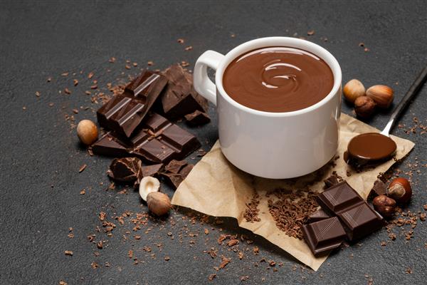 فنجان شکلات داغ و تکه های شکلات روی زمینه بتن تیره