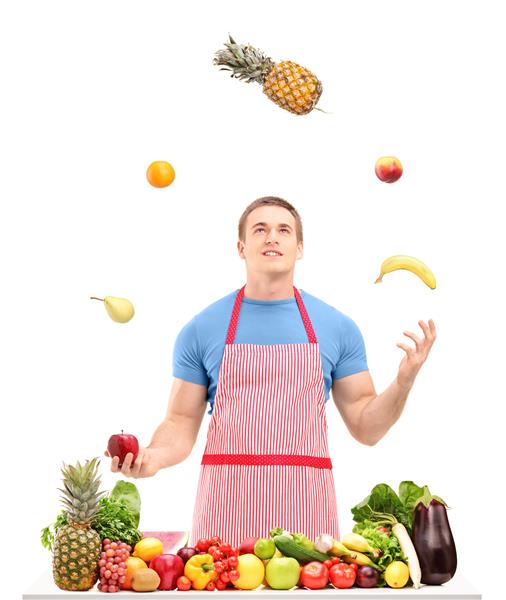 مردی در پشت میز پر از میوه و سبزیجات جدا شده روی پس زمینه سفید با میوه ها دست و پنجه نرم می کند