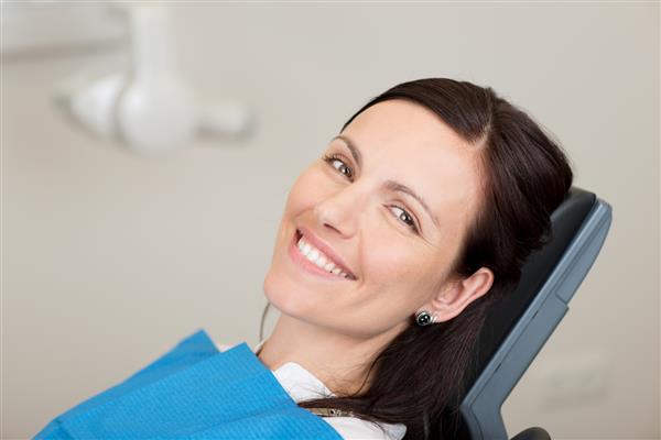 پرتره یک بیمار زن بالغ میانی که در دندانپزشکی لبخند می زند