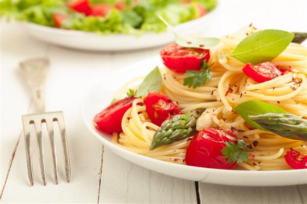 ماکارونی اسپاگتی گیاهی با نیزه های مارچوبه سبز تازه گوجه فرنگی و گیاهانی که همراه با سالاد سبز برگ دار سرو می شوند