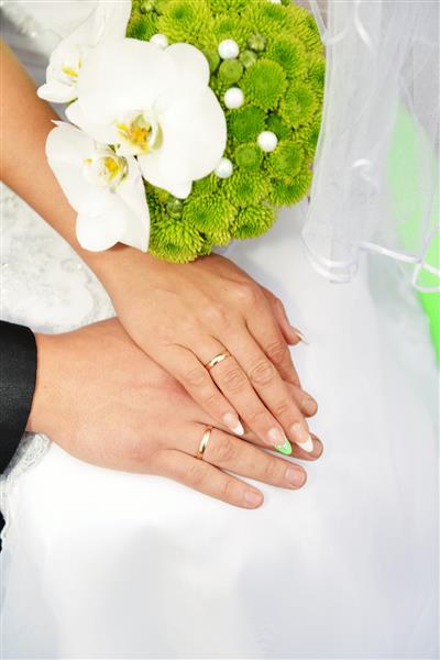 دستهایی با حلقه های ازدواج و دسته گل از گل ارکیده سفید