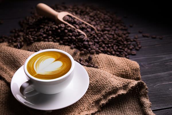 فنجان قهوه لاته با شکل قلب و دانه های قهوه در زمینه چوبی قدیمی