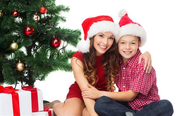 تعطیلات هدیه کریسمس مفهوم - مادر و کودک پسر خوشحال در کلاه های کمکی سانتا با جعبه های هدیه