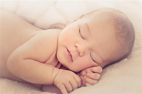 پرتره نوزاد پسر تازه متولد شده روی پوشش نرم بژ خوابیده است