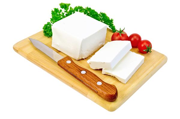 پنیر فتا چاقو جعفری و گوجه فرنگی روی تخته چوبی که روی زمینه سفید قرار دارد