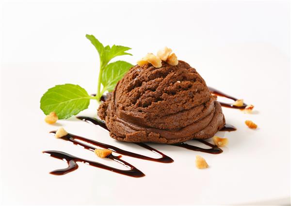 یک قاشق بستنی شکلاتی تیره تزئین شده با آجیل و سس شکلات