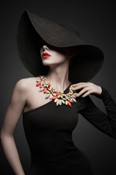 پرتره مدل خانم جوان با کلاه سیاه زیبا و لباس شب زن شیک با جواهرات مدرن عکس استودیویی از مدل زیبا در پس زمینه خاکستری