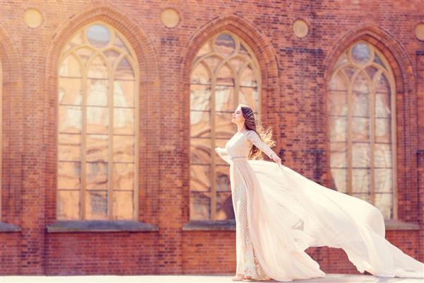 عروس در زمینه کلیسا مدل مد ظریف در پرتره زیبایی لباس بلند سفید لباس پرواز تکان دهنده در باد