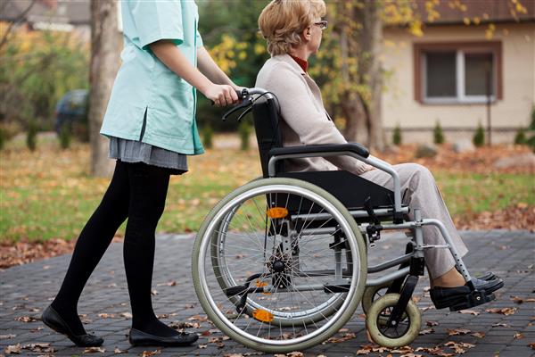مراقب در یک پیاده روی آرام با زن مسن روی صندلی چرخدار