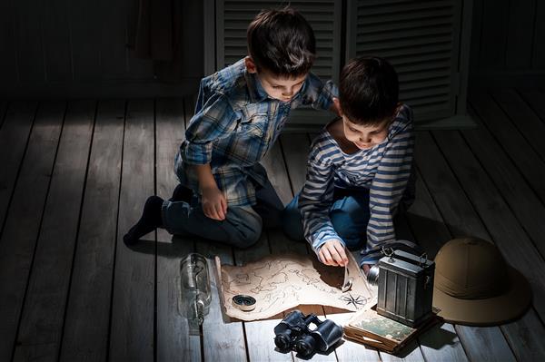 دو پسر شب هنگام با چراغ قوه در حال مطالعه نقشه قدیمی اتاق خود هستند