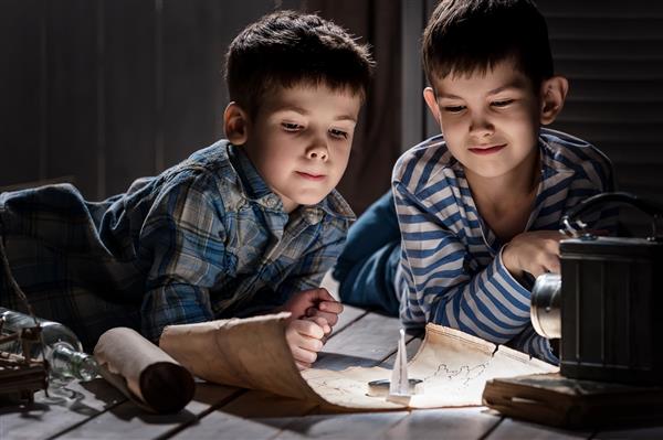 دو پسر شب هنگام با چراغ قوه در حال مطالعه نقشه قدیمی اتاق خود هستند