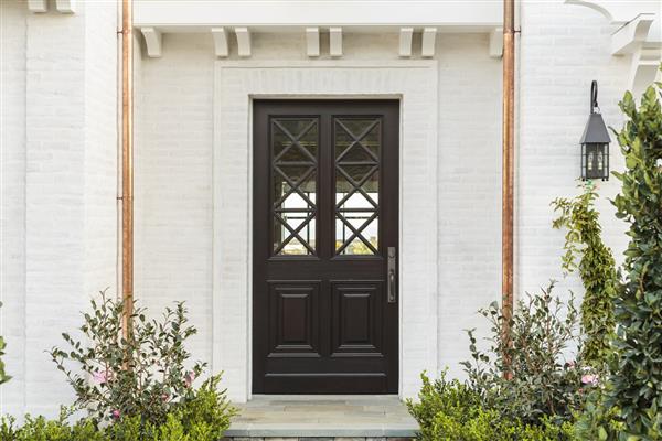 افقی درب ورودی چوبی پیچیده به یک خانه خانوادگی درب دارای الگوهای متقاطع است خانه آجر سفید شده است جزئیات لوله های تخلیه مس خانه گیاهان و مرحله جلو نیز دیده می شود