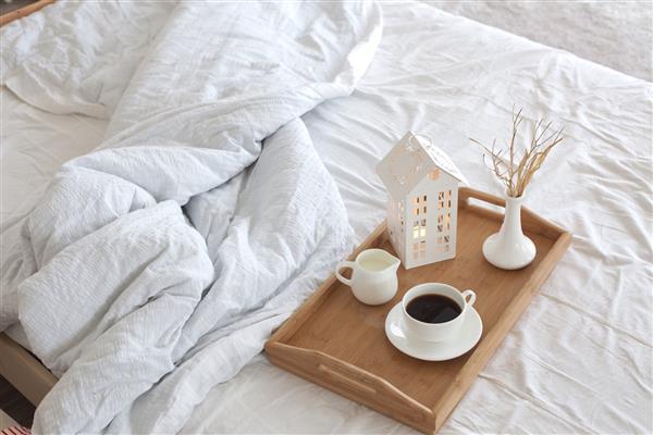 سینی چوبی با قهوه و دکوراسیون داخلی روی تخت با پارچه سفید