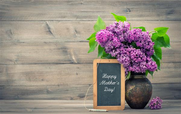 دسته گل گل یاسی در گلدان روی زمینه چوبی تخته سیاه با متن نمونه روز مادر مبارک سبک برش خورده تصویر