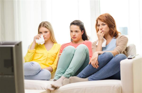 خانه فناوری و مفهوم دوستی - سه دختر نوجوان غمگین که در خانه تلویزیون تماشا می کنند