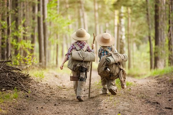 دو پسر با کوله پشتی ها در یک جاده جنگلی و یک روز آفتابی به پیاده روی می روند
