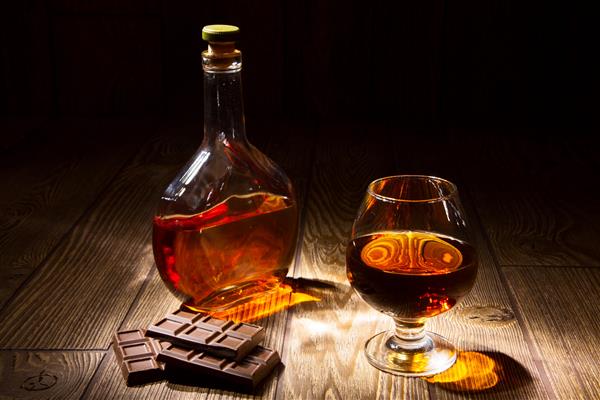یک بطری و یک لیوان براندی با شکلات روی میز چوبی
