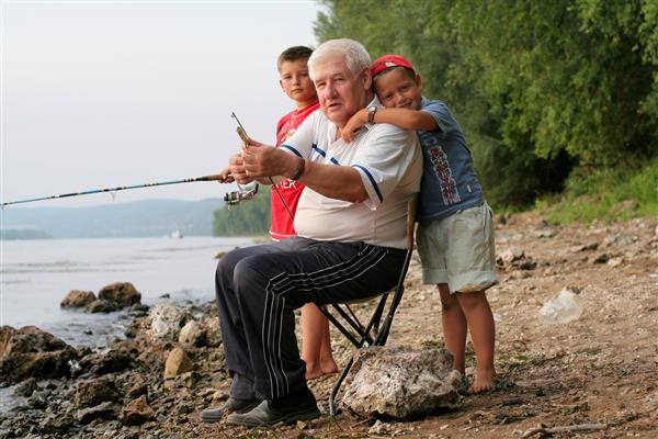 یک پدربزرگ سر خاکستری به همراه دو نوه در حال ماهیگیری