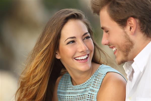 زن و شوهر بامزه ای که با لبخندی کامل و سفید می خندند و در فضای باز با پس زمینه ای متمرکز به یکدیگر نگاه می کنند