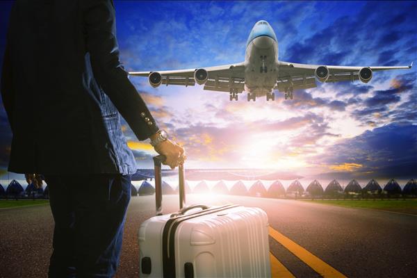 مرد تجاری و چمدان ایستاده در فرودگاه و هواپیمای جت مسافربری که بر فراز باند پرواز می کند در برابر آسمان زیبا برای حمل و نقل هوایی و سفر با موضوع هواپیمایی
