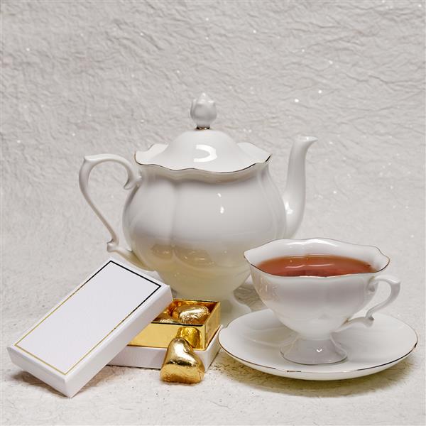 قوری چینی سفید و یک فنجان چای و یک جعبه آبنبات طلا