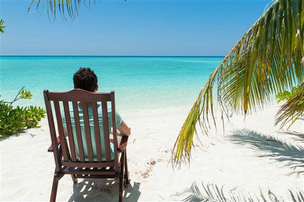 مردی که روی صندلی کنار درختان نخل جزایر مالدیو استراحت می کند