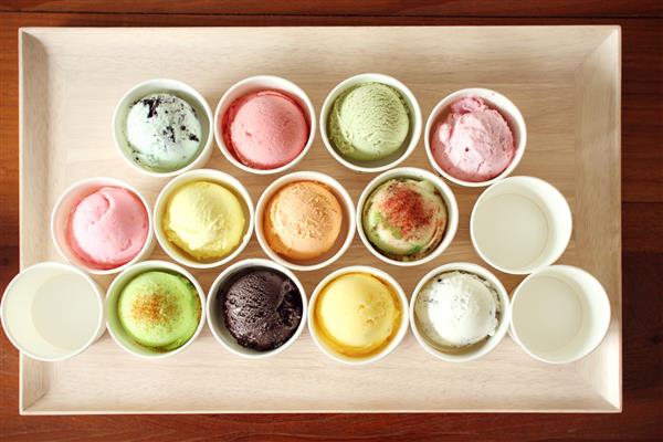 قاشق های بستنی شیرین و رنگارنگ روی بشقاب چوبی