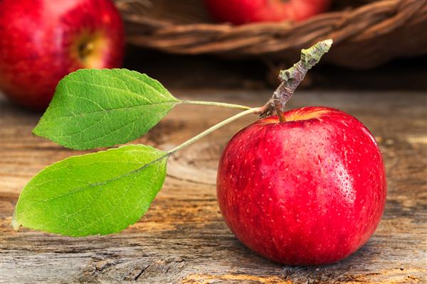 سیب قرمز براق با ساقه و برگهای سبز روی چوب های روستایی مفاهیم مزرعه به میز انتخاب سالم دسر ناهار مدرسه