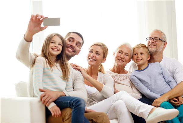 خانواده خوشبختی نسل و مفهوم مردم - خانواده ای خوشحال که روی کاناپه نشسته و با گوشی هوشمند در خانه سلفی می گیرند