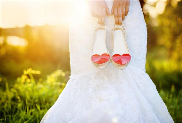 عکس عروس غیرقابل شناسایی که کفش های عروسی را با قلب های قرمز در دست دارد