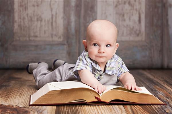 خواندن نوزاد پسر شایان ستایش که روی زمین دراز کشیده و مشغول خواندن یک کتاب غول پیکر است