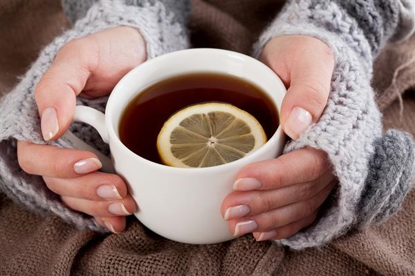 دست زن و فنجانی چای با لیمو در یک روز سرد