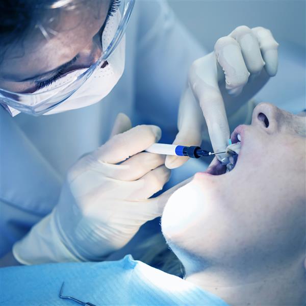 دندانپزشکی که یک بیمار زن را معالجه می کند