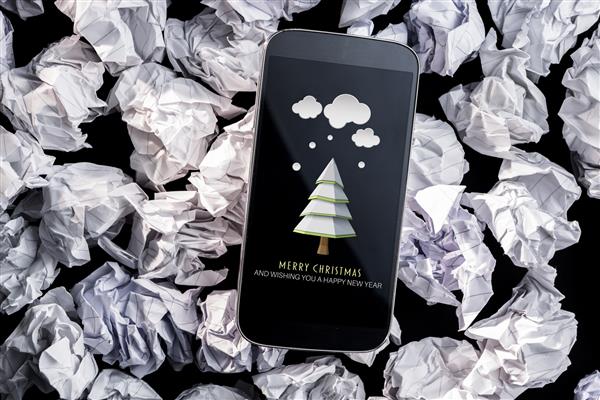 درخت صنوبر با برف در برابر تلفن هوشمند روی کاغذ مچاله شده