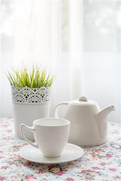 مجموعه ای از فنجان و قوری چای کنار پنجره