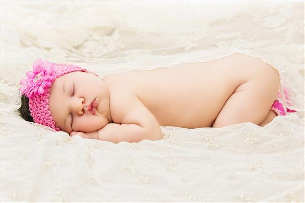 کودک تازه متولد شده با دکوراسیون گل روی سربند با آرامش خوابیده است