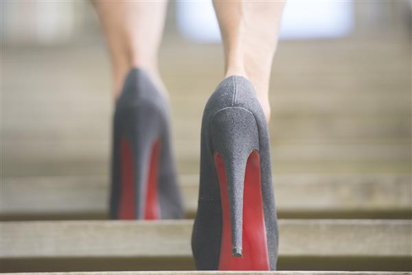 جزئیات مربوط به نمای رو به بالا از زن با کفش های استیلت پاشنه بلند که از پله های چوبی با پس زمینه تار بالا می رود