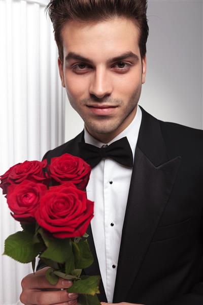 یک مرد در حالی که دسته گلهای قرمز را در دست داشت به دوربین لبخند می زد