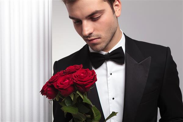 یک مرد که دسته گلهای قرمز را در دستان خود گرفته و به ستون سفید تکیه داده است