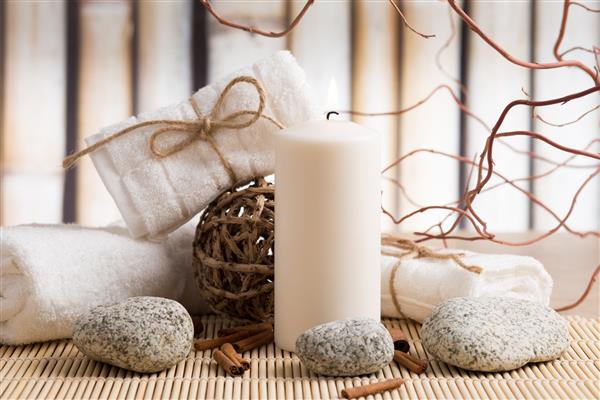 ترکیبی از درمان آبگرم شمع حوله ها و سنگ های گرم در زمینه بامبو