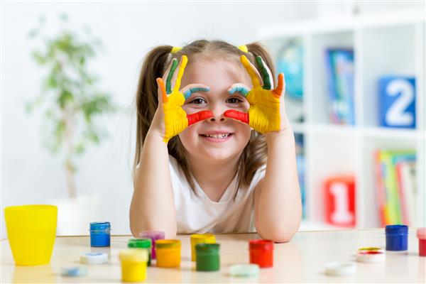 دختر بچه شاد و ناز نشان دادن دستان خود را با رنگ های روشن نقاشی کرده است