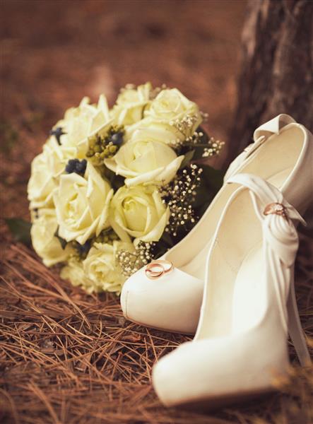 تصویری از کفش عروس سفید زنانه با دسته گل روی چمن های سبز