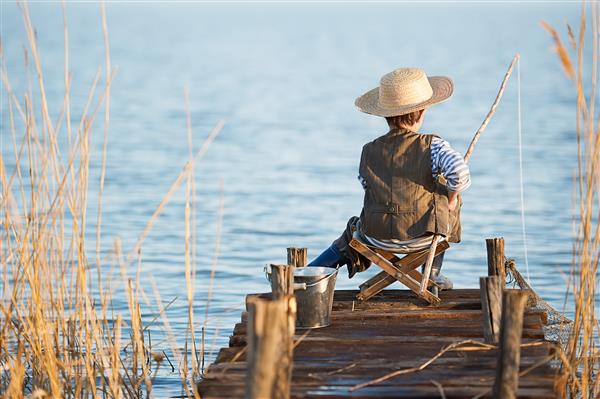 پسر کوچک هنگام غروب خورشید در دریاچه مشغول ماهیگیری است