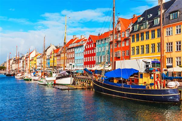 نمای زیبا و تابستانی اسکله نیهاون با ساختمانهای رنگی کشتی ها قایق های تفریحی و قایق های دیگر در شهر قدیمی کپنهاگ دانمارک