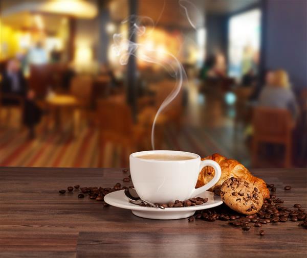 نوشیدنی قهوه همراه با کروسان روی میز چوبی که دارای کافه تریای تاریک است