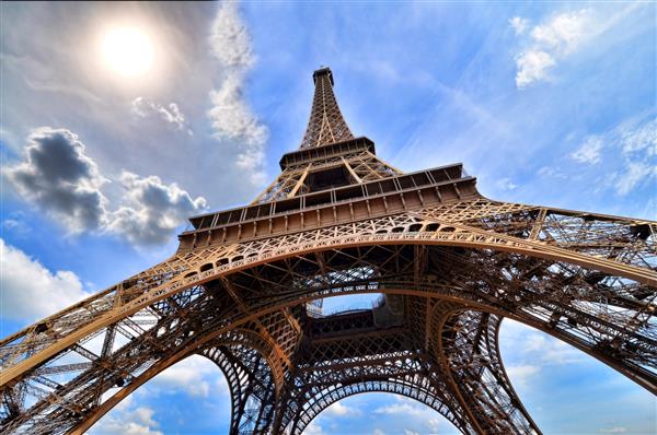 برج ایفل پاریس فرانسه نمای رو به بالا با خورشید و آسمان آبی پر جنب و جوش