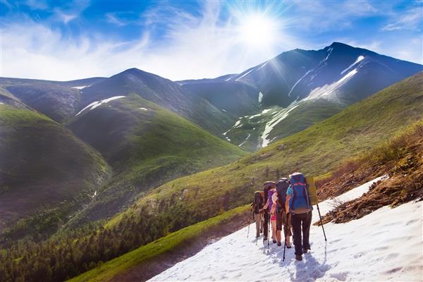 گروهی از دوستان در پیاده روی در کوههای بلند قله های پوشیده از برف یخچال های طبیعی و پس زمینه آسمان خارق العاده با ابرهای آبی دنیای زیبا